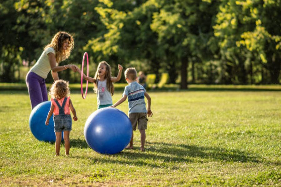 Group of kids and teacher playing with a sports balls in nature.